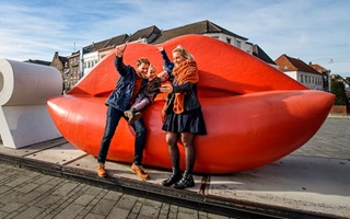 Gezin poseert bij het kunstwerk met rode lippen tijdens de Virtual Adventure Tour in Roermond, een interactieve stadswandeling voor kinderen.