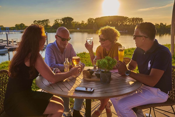 Two women and men enjoy the setting sun on the terrace of Maas Residence Thorn