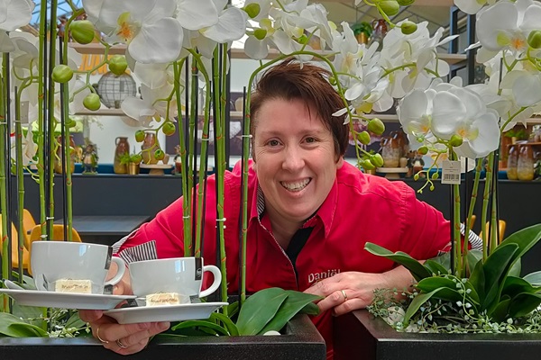 Medewerker van Tuincentrum Daniëls poseert met twee kopjes koffie voor de foto tussen de planten en het groen van het tuincentrum