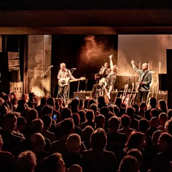 Optreden van een rockband bij Popodium de Bosuil in Weert waar het publiek massaal aanwezig is en de gitarist naar bovens wijst.
