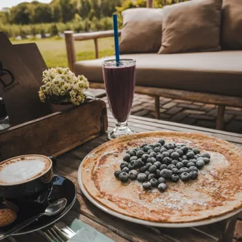 Verse pannenkoek met blauwe bessen, smoothie en cappuccino op het terras van Plantage Blankwater, met uitzicht op de herfstige bessenvelden in Limburg.