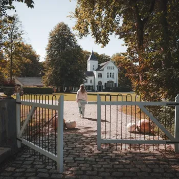Vrouw loopt over de oprijlaan richting Kasteel Frymerson, omgeven door bomen en herfstlicht.