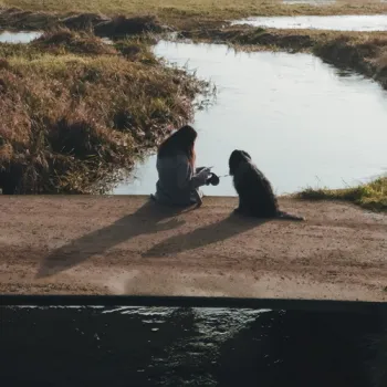 Vrouw en hond zitten op een knuppelbrug met uitzicht over het water